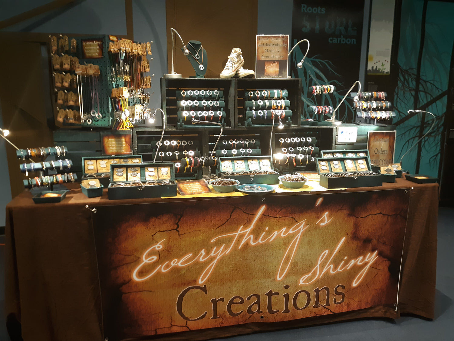 Booth setup for Everything's Shiny Creations, showcasing a variety of hand-stamped jewelry and accessories.  